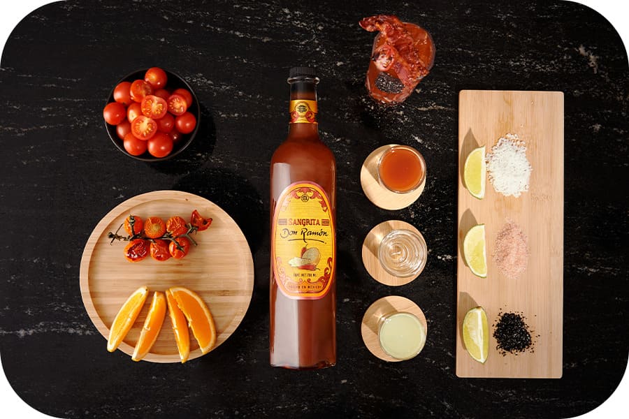 Sangrita Don Ramón y aperitivos sobre mesa oscura.